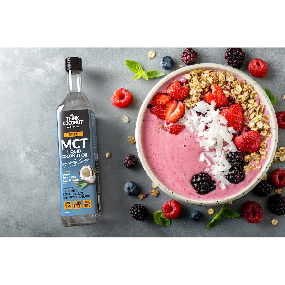Think Coconut MCT Liquid Coconut Oil bottle beside a berry smoothie bowl topped with strawberries, blackberries, granola and coconut flakes